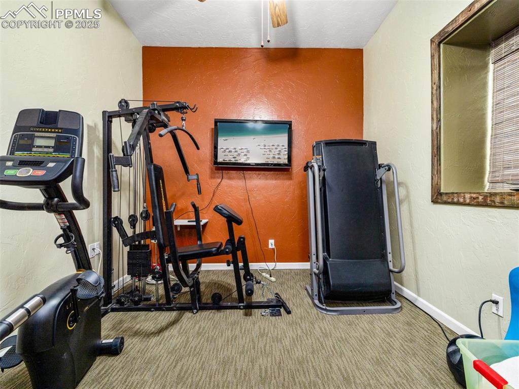 Image 32 of 46: Exercise room with a textured wall, carpet flooring, and ceiling fan