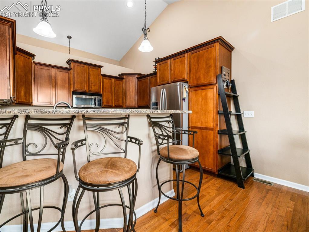 Image 6 of 46: Kitchen with a breakfast bar area, pendant lighting, brown cabinetry, appli