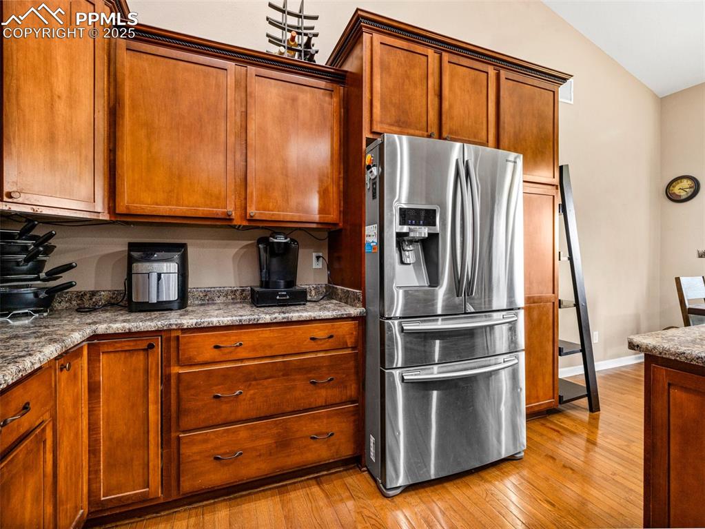 Image 9 of 46: Kitchen with stainless steel fridge with ice dispenser, brown cabinetry, li