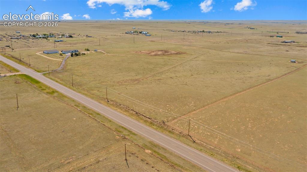 Image 33 of 40: Expansive open land with a paved road, scattered structures, and clear skie