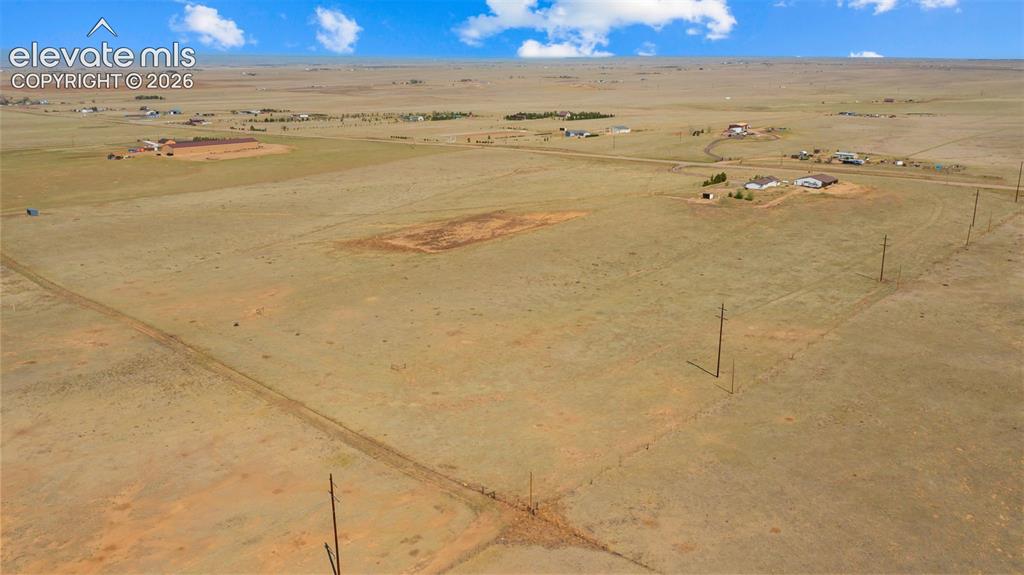 Image 35 of 40: Expansive open land featuring a dirt road, scattered structures, utility po