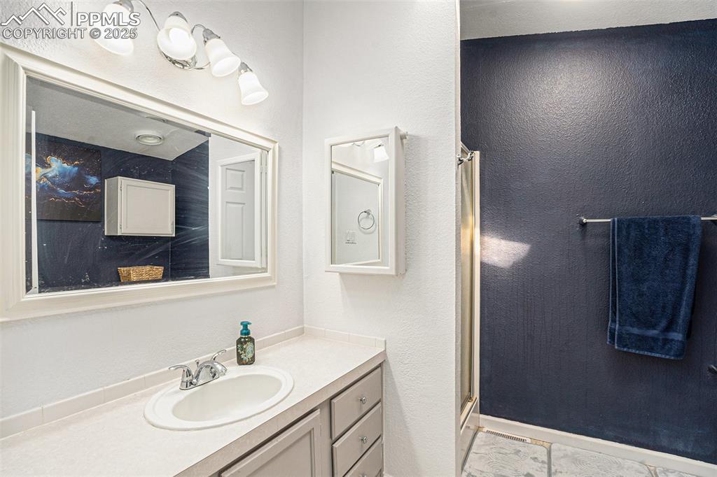 Image 16 of 24: Bathroom with a stall shower, vanity, a textured wall, and light tile patte