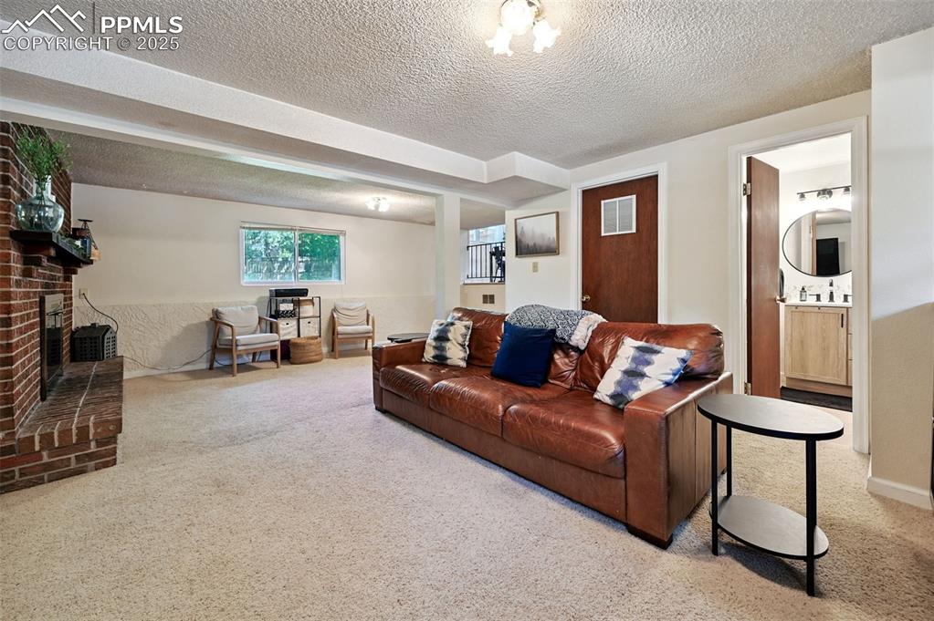 Image 18 of 31: Living area featuring carpet floors, a textured ceiling, and a brick firepl