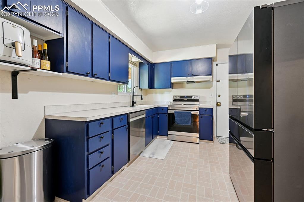Image 9 of 31: Kitchen with appliances with stainless steel finishes, blue cabinets, under
