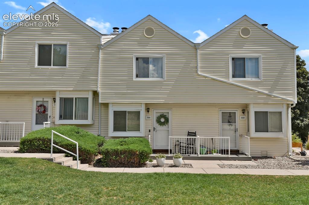 Caption: Cream-colored siding exterior with a front walkway, mature landscaping, and an individual entrance