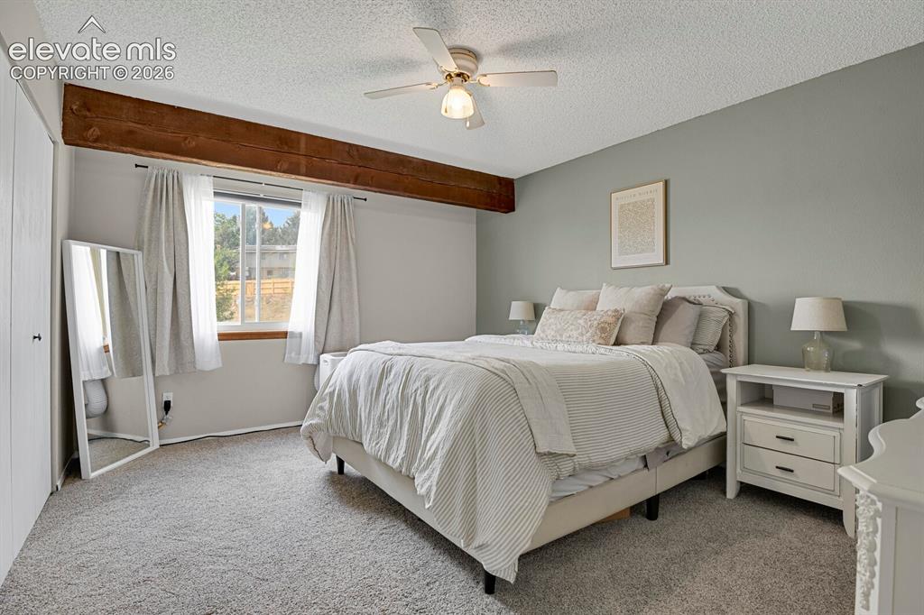 Image 16 of 32: Ceiling fan light fixture, exposed wood beam, window with white trim, and l