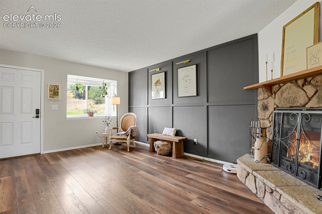 Image 5 of 32: Stone-clad fireplace with a wood mantel, wood-finish flooring, and a decora