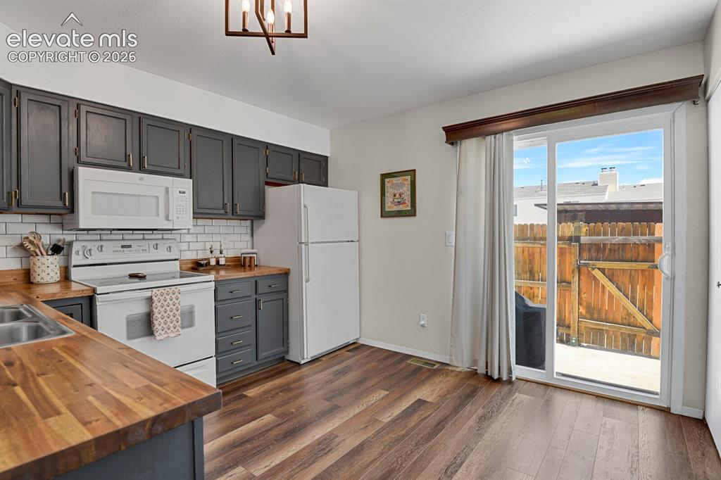 Image 8 of 32: White appliances, wood-finish flooring, dark gray cabinetry with gold hardw