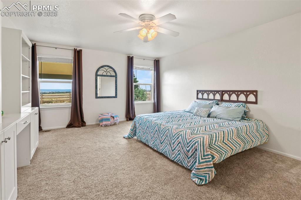 Image 14 of 32: Bedroom with light colored carpet and a ceiling fan