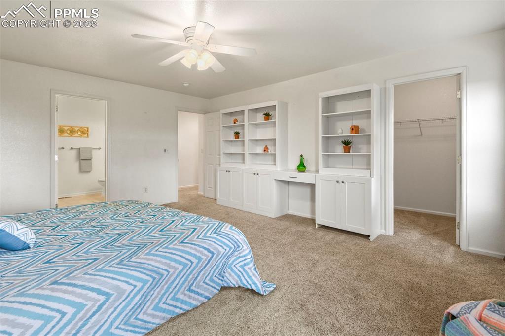 Image 16 of 32: Bedroom with a walk in closet, light carpet, ceiling fan, and ensuite bathr