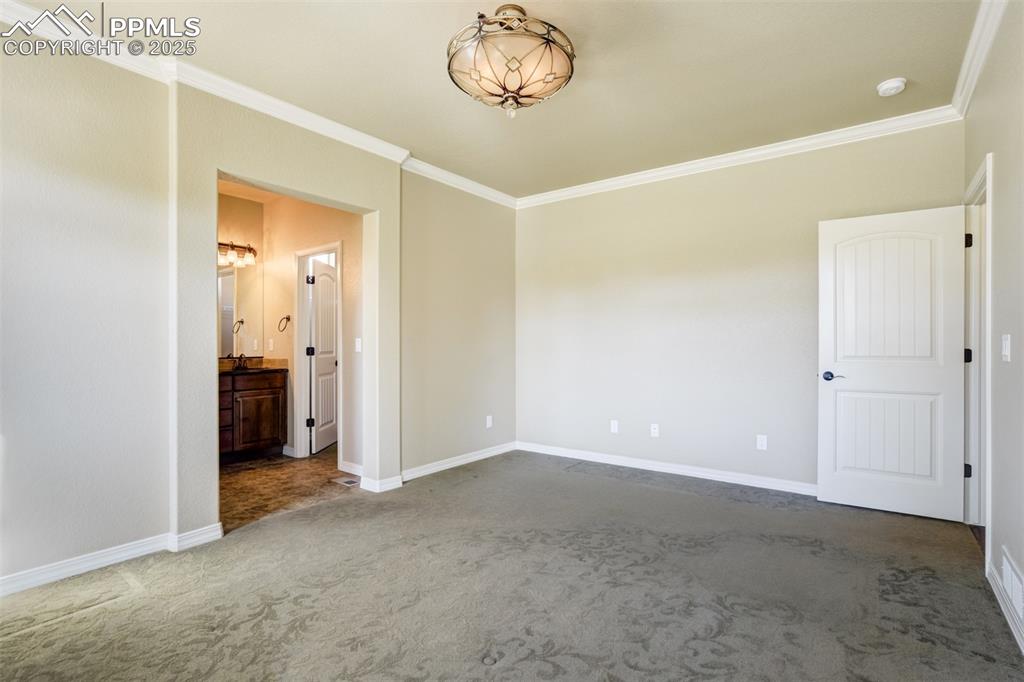 Image 13 of 36: Unfurnished bedroom with ornamental molding, carpet flooring, and ensuite b