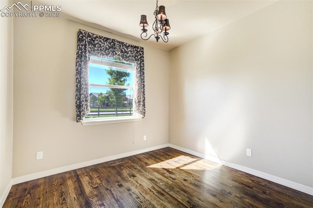 Image 17 of 36: Unfurnished room featuring a chandelier and dark wood-type flooring