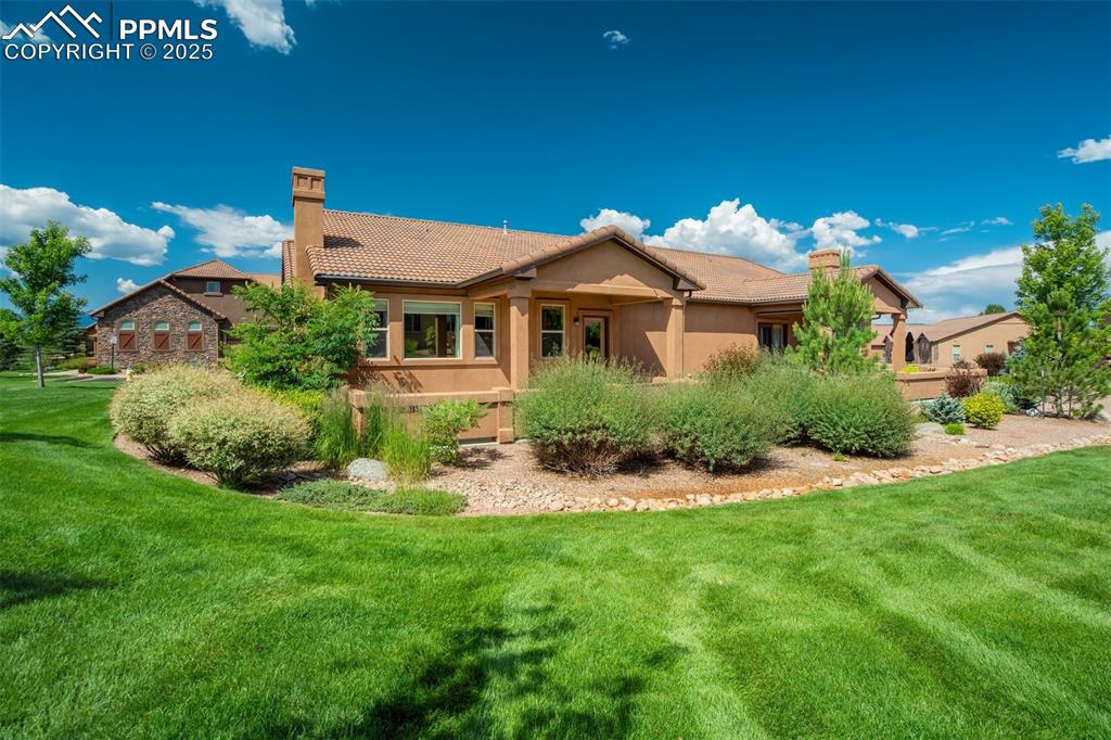 Image 27 of 36: Back of property featuring a chimney, stucco siding, a yard, and a tiled ro