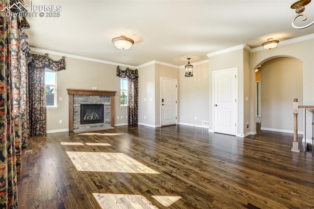 Image 6 of 36: Unfurnished living room with arched walkways, a fireplace, wood finished fl