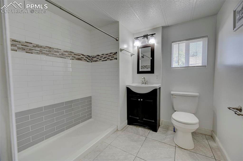 Image 16 of 26: Bathroom featuring vanity, a tile shower, a textured ceiling, and tile patt