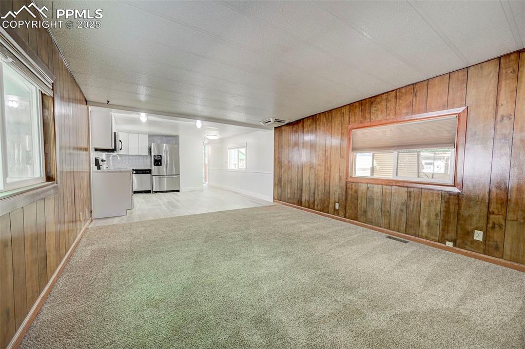 Image 3 of 26: Unfurnished living room featuring wooden walls and light carpet