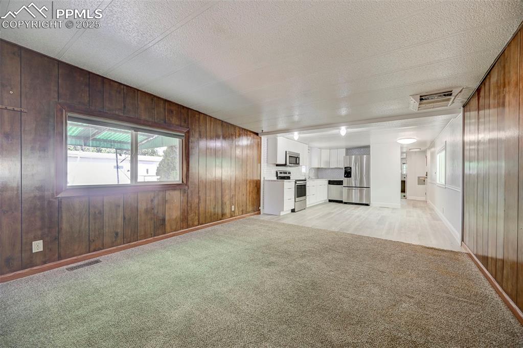 Image 4 of 26: Unfurnished living room featuring light colored carpet, wood walls, and a t