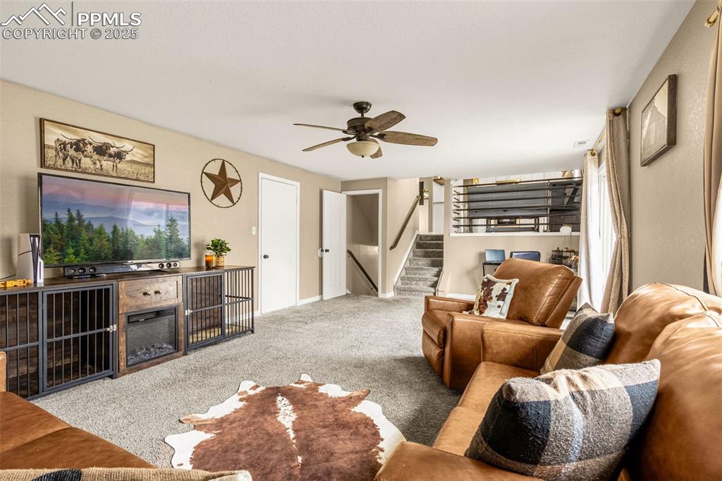 Image 12 of 34: Carpeted living area with stairway and a ceiling fan