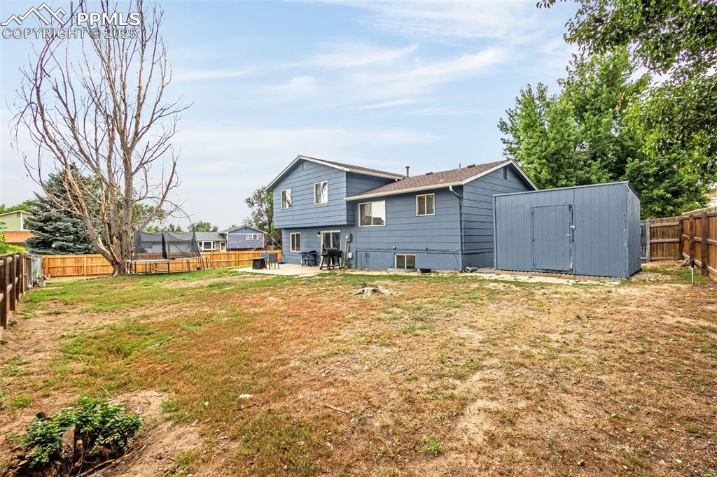 Image 27 of 34: Rear view of house featuring a fenced backyard, a storage unit, a trampolin