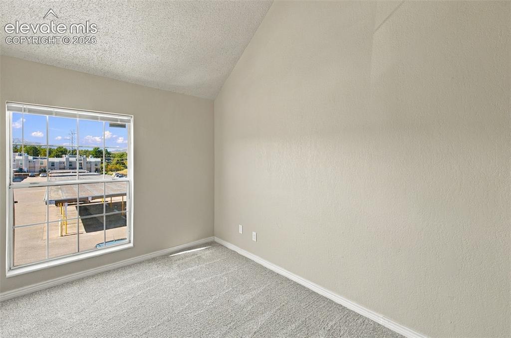 Image 15 of 26: Vaulted ceiling, neutral wall paint, carpeted flooring, large window with b