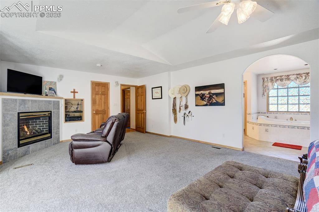 Image 20 of 50: Living area featuring ceiling fan, carpet, a tiled fireplace, vaulted ceili