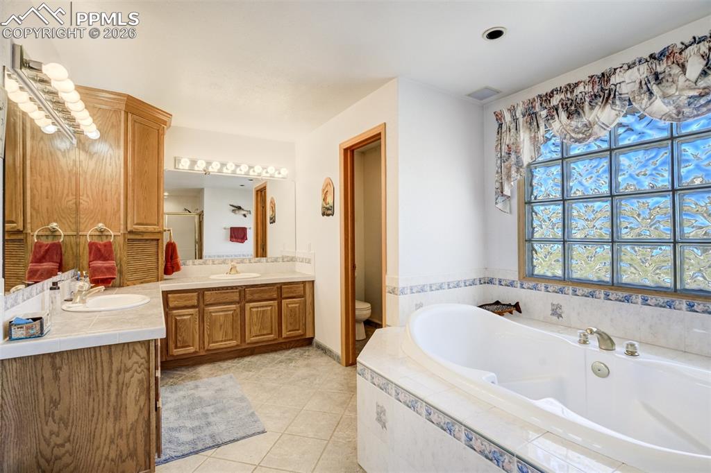 Image 23 of 50: Bathroom with vanity, light tile patterned floors, and a garden tub