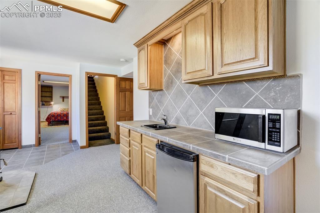 Image 34 of 50: Kitchen featuring light colored carpet, light wood finish cabinetry, stainl