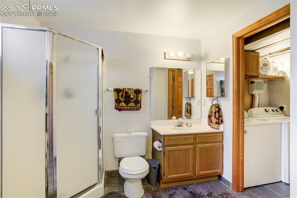 Image 41 of 50: Bathroom with vanity, a stall shower, washer and dryer, and dark tile patte