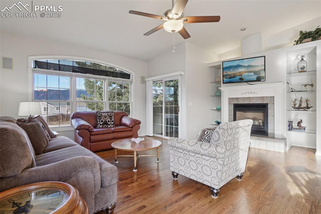 Image 6 of 42: Living area with natural wood flooring, ceiling fan, a fireplace, built in