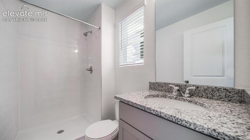 Image 18 of 24: Bathroom featuring a white subway tile shower, a granite-finish countertop,