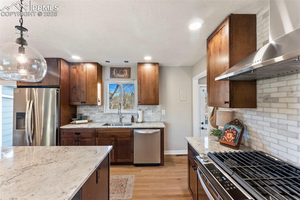 Image 12 of 45: Kitchen featuring stainless steel appliances, wall chimney range hood, ligh