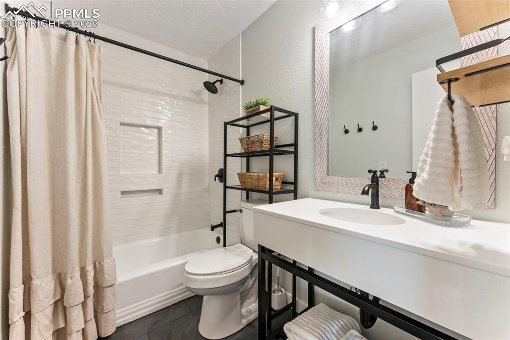 Image 15 of 45: Bathroom featuring shower / bathtub combination with curtain and dark tile