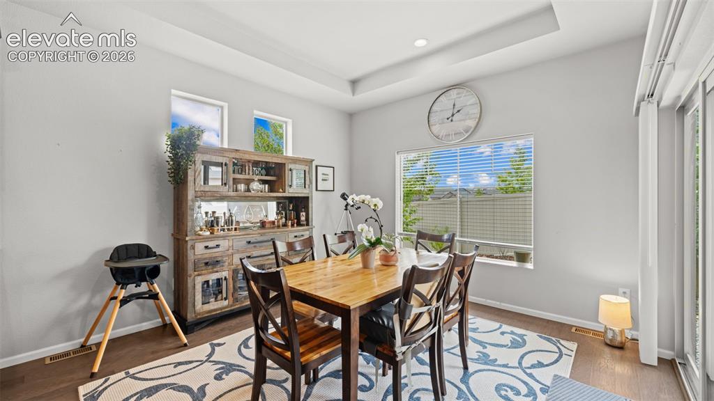 Image 13 of 34: Spacious room featuring wood-finish flooring, a tray ceiling, and multiple