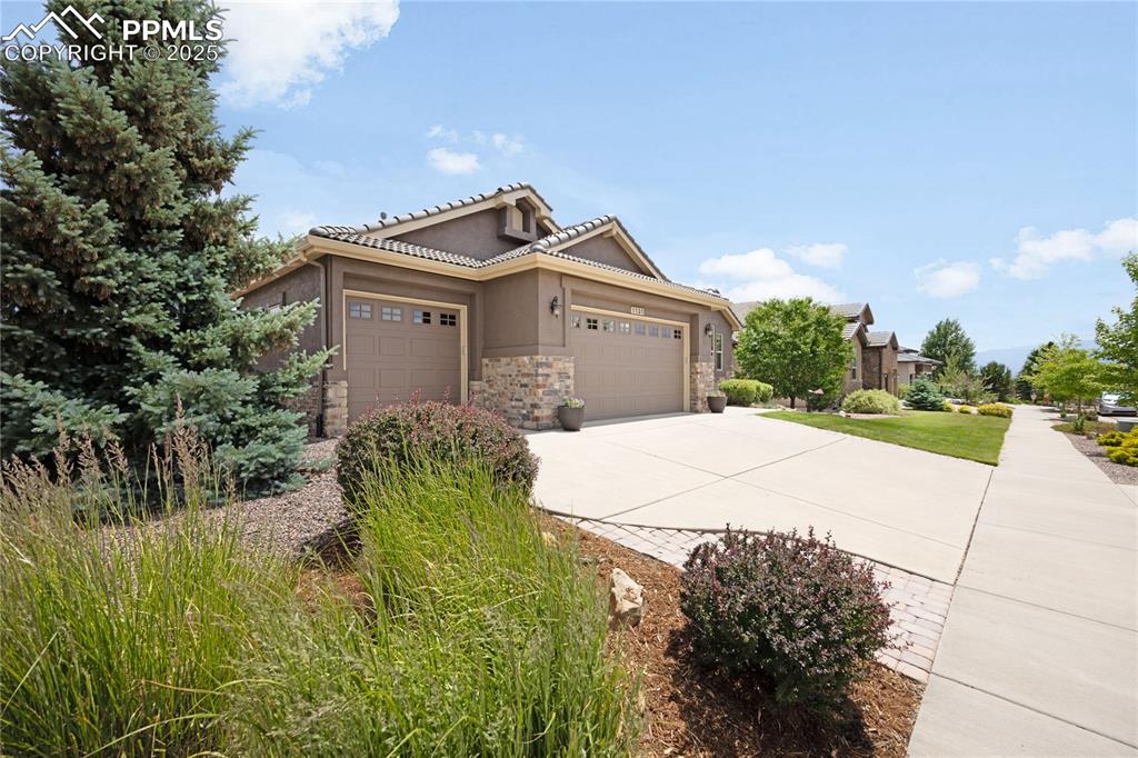 Image 37 of 39: View of front of home with an attached garage, stone siding, concrete drive