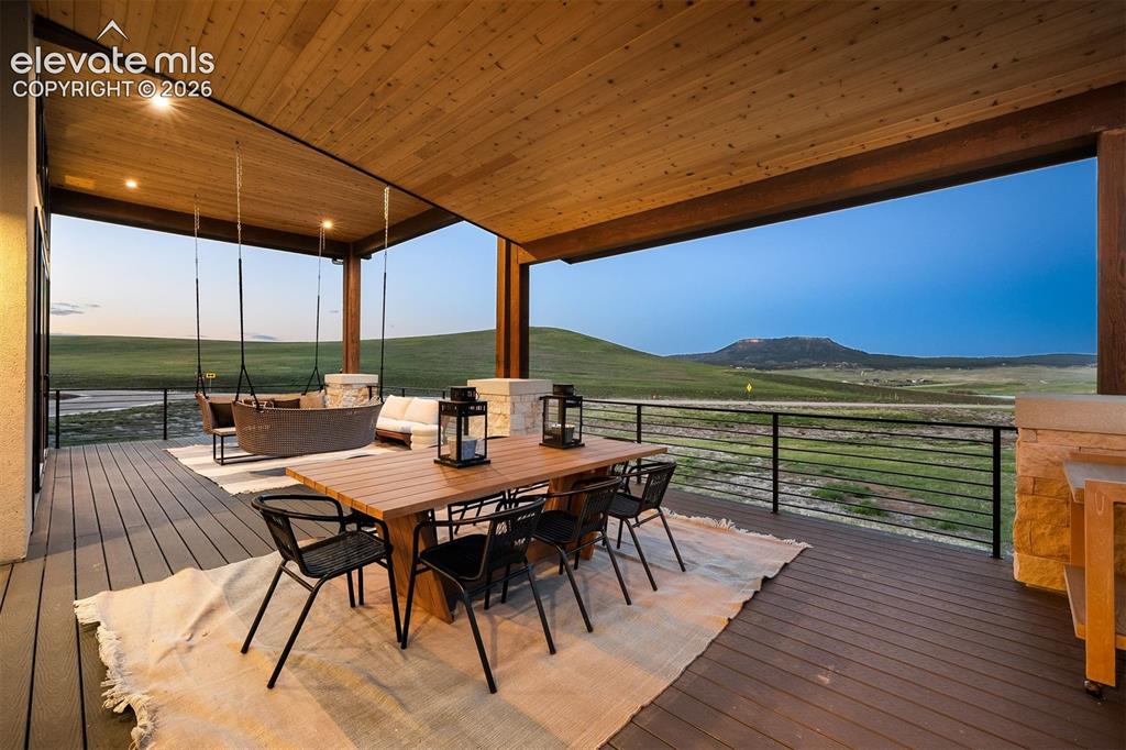 Image 16 of 38: Covered deck with wood-paneled ceiling, stone columns, and panoramic sunset