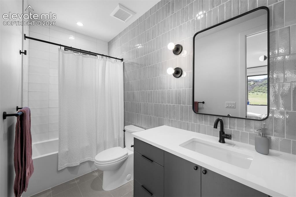 Image 27 of 38: Bathroom finished with full-height tile surround and quartz countertop.