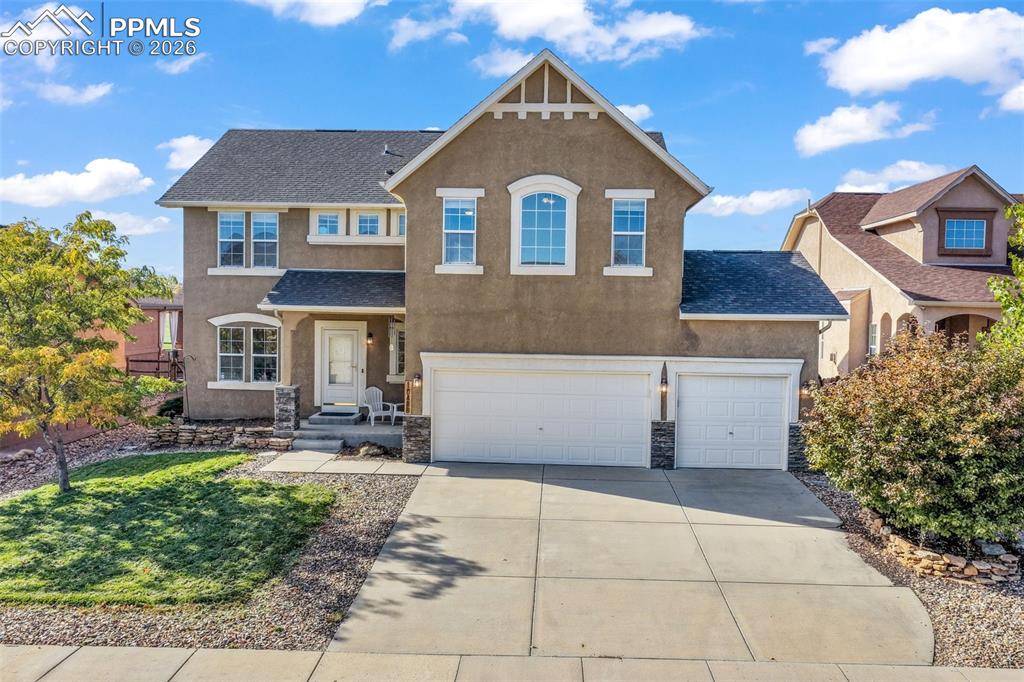 Caption: View of front of house featuring stucco siding, roof with shingles, concrete driveway, stone siding,