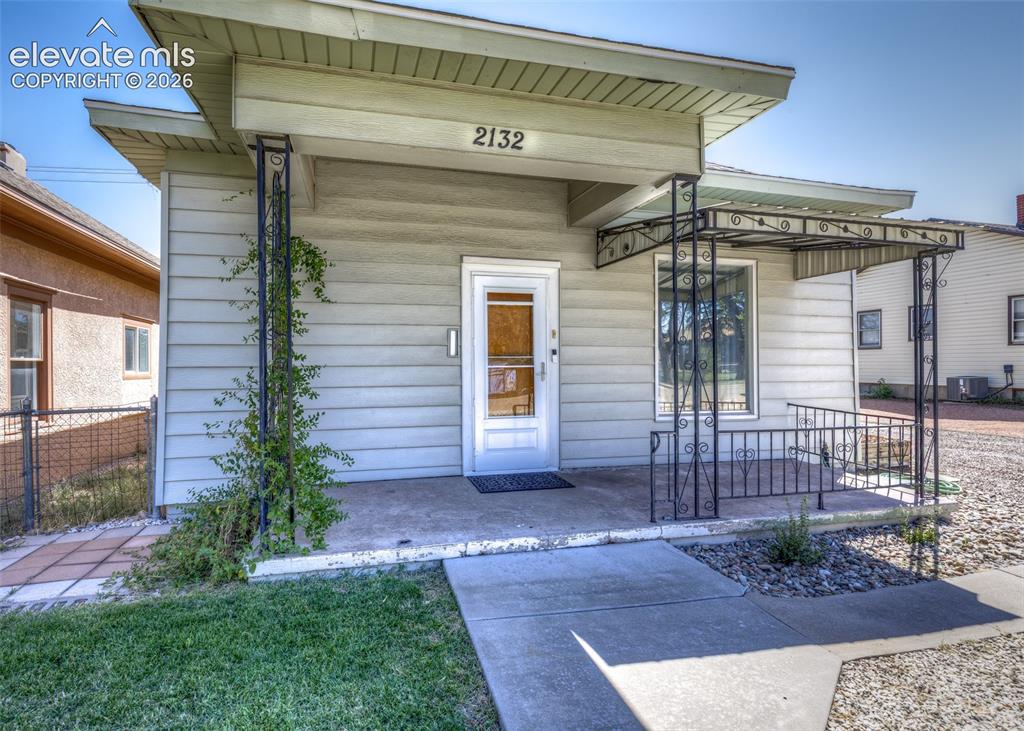 Caption: Front entry with decorative wrought iron porch railing, covered porch, and concrete walkway