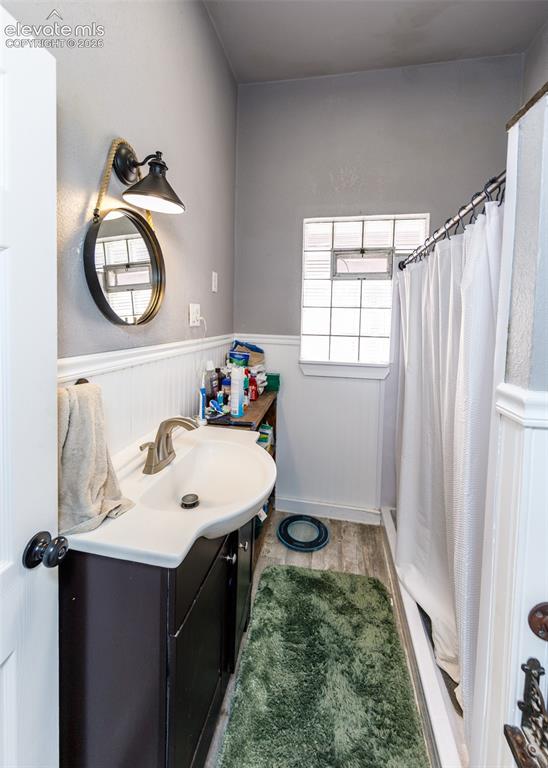 Image 17 of 25: Vanity with integrated sink, wood-finish flooring, white wainscoting, and g