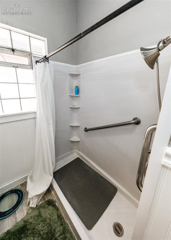 Image 18 of 25: Shower with grab bar, built-in corner shelving, and a handheld shower head