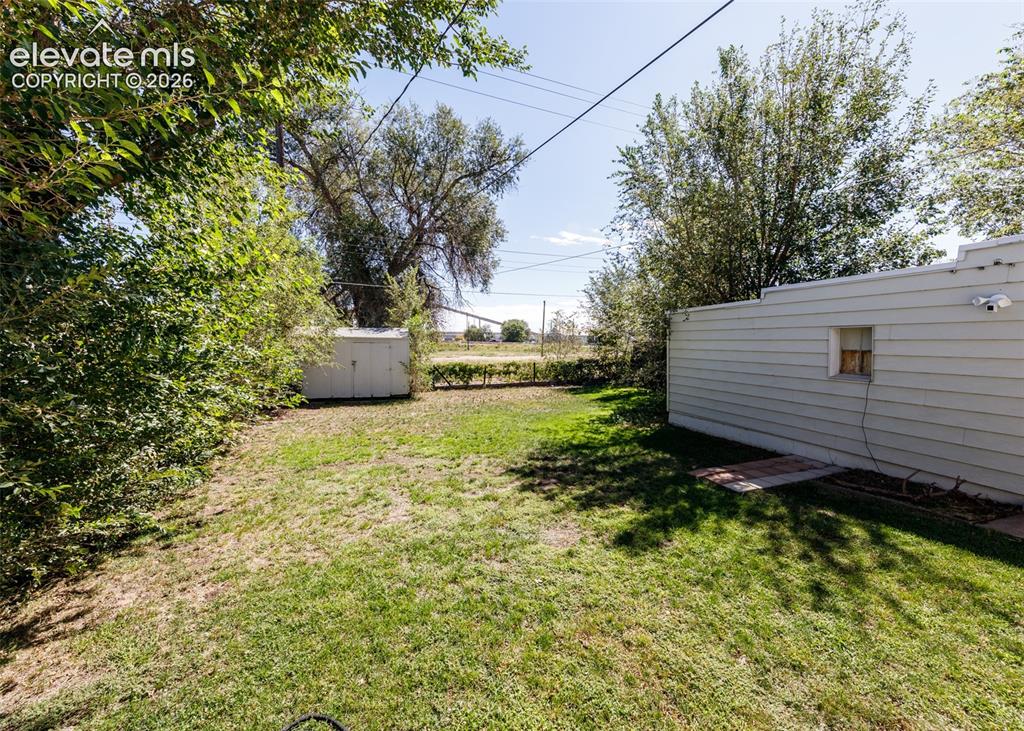 Image 20 of 25: Expansive grassy area with established trees and a storage shed