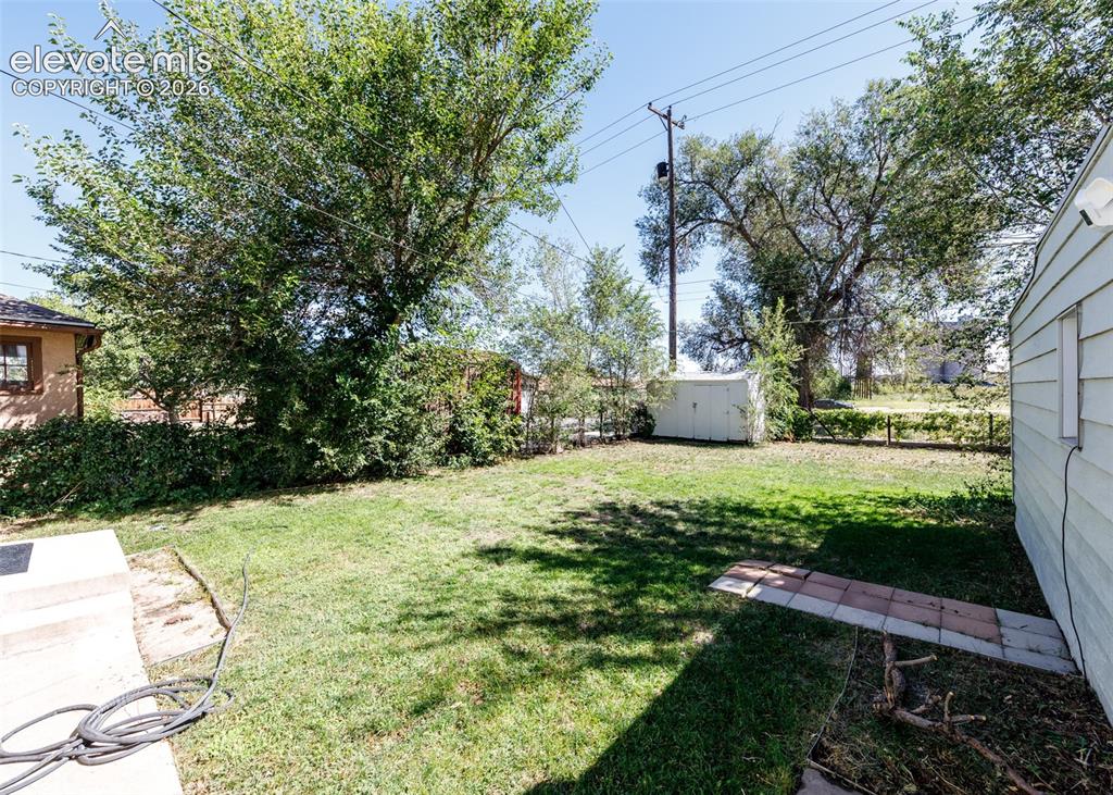 Image 21 of 25: Expansive yard featuring a grass lawn, mature trees, and a storage shed
