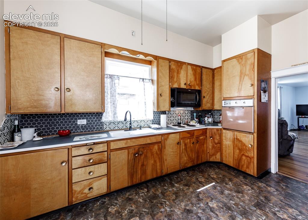 Image 6 of 25: Wood-finish cabinetry with brass-tone hardware, dark hexagonal tile backspl