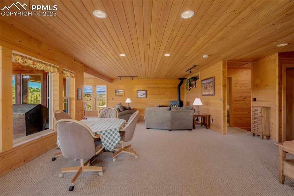 Image 12 of 48: Dining room with a wood stove, carpet flooring, wood walls, recessed lighti