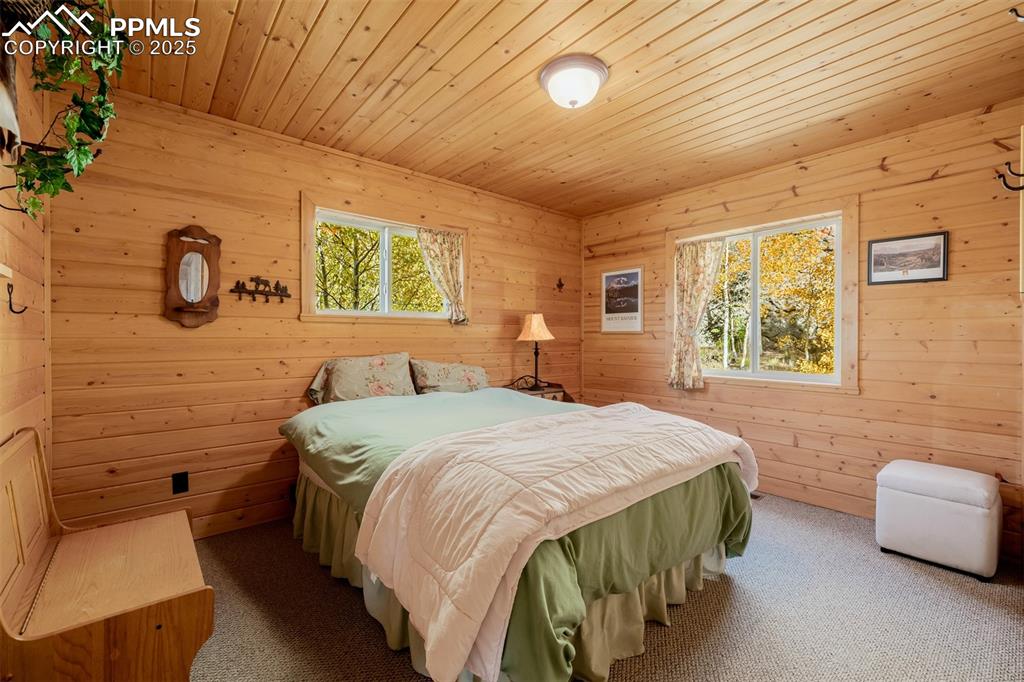 Image 21 of 48: Bedroom with carpet flooring, wooden walls, wooden ceiling, and multiple wi