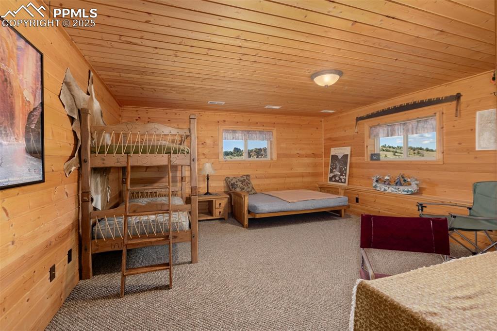 Image 23 of 48: Bedroom with wooden ceiling, wood walls, carpet flooring, and multiple wind