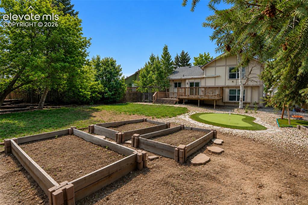Image 1 of 35: View of the back of the home with putting green, deck, and raised gardening