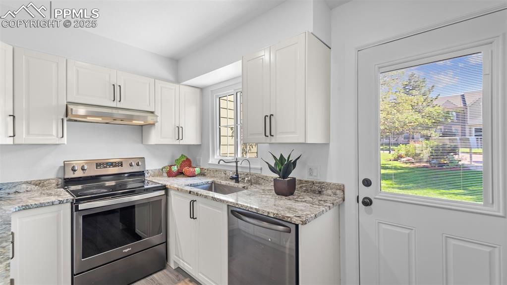 Image 10 of 21: Kitchen with stainless steel appliances, white cabinets, light stone counte