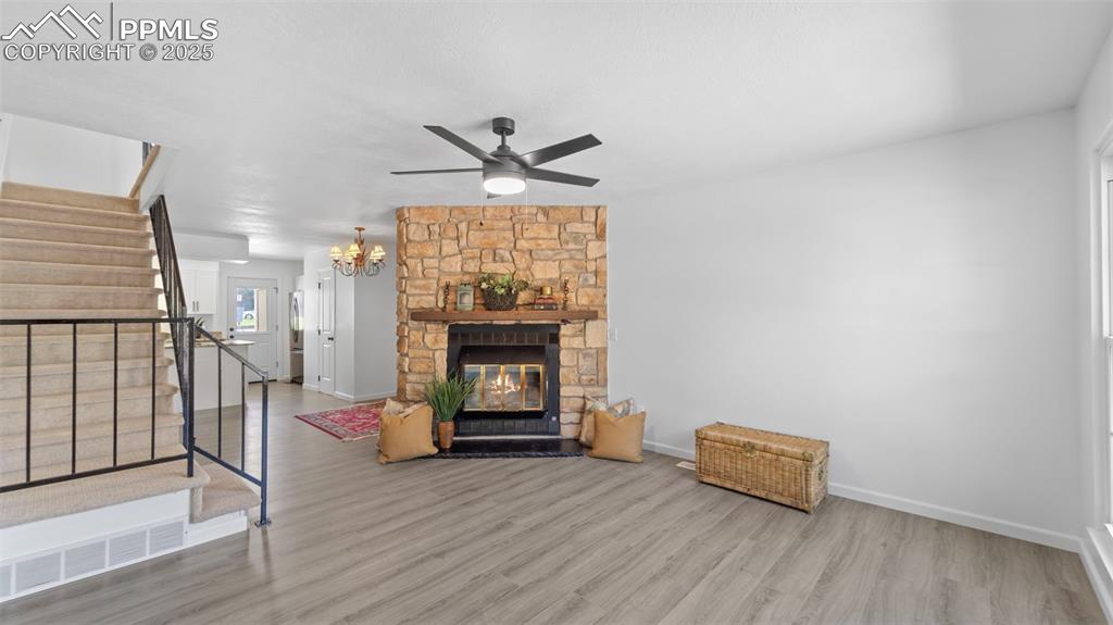 Image 4 of 21: Living room with stairs, wood finished floors, a stone fireplace, ceiling f