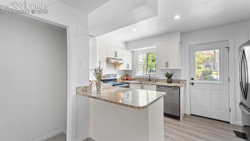 Image 8 of 21: Kitchen featuring a peninsula, light stone counters, white cabinets, applia